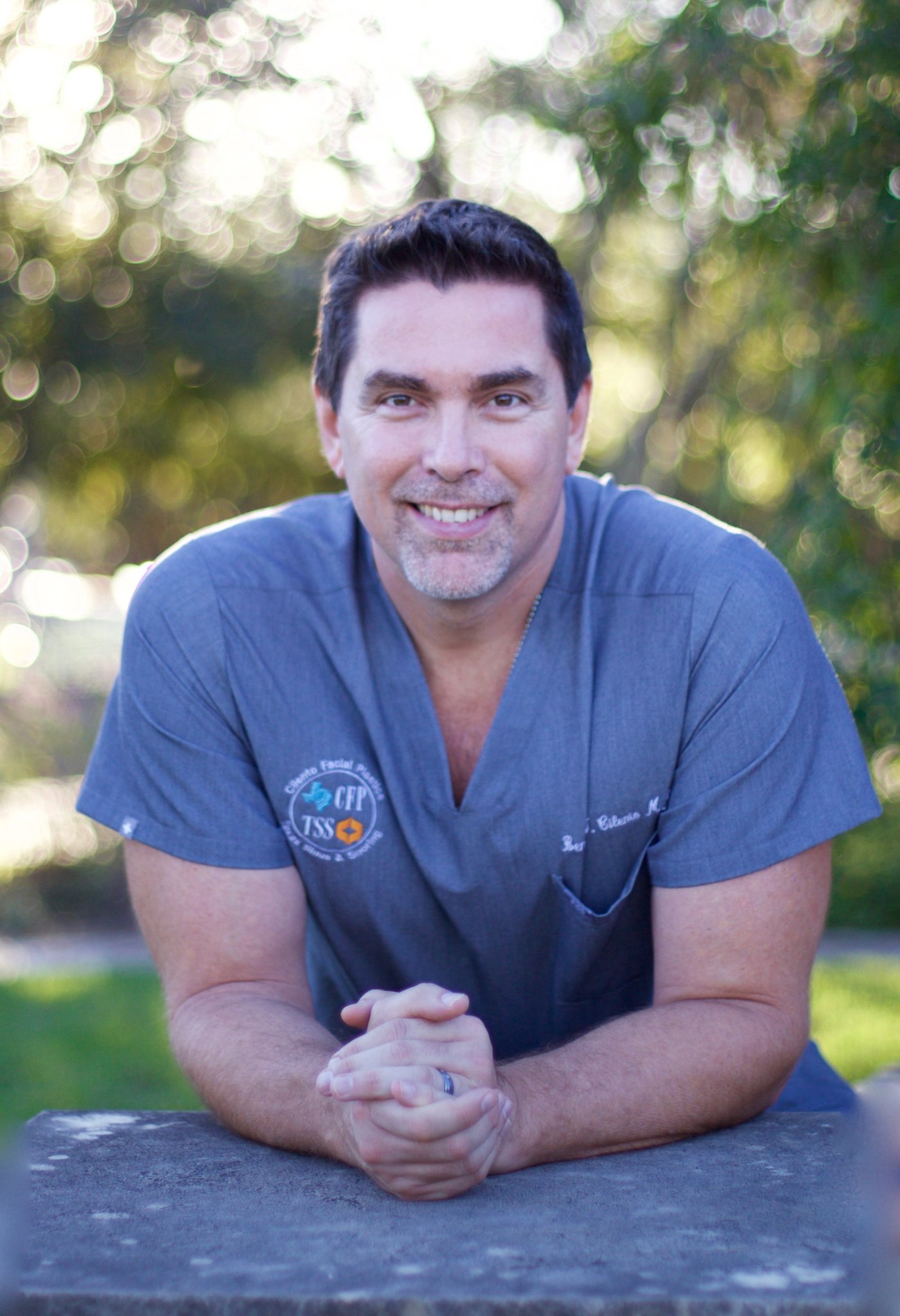 Dr. Ben Cilento, ENT surgeon, smiling outdoors in blue scrubs